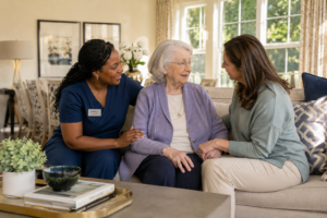 Caregiver and adult daughter sitting peacefully with a woman receiving hospice support in a residential memory care home.